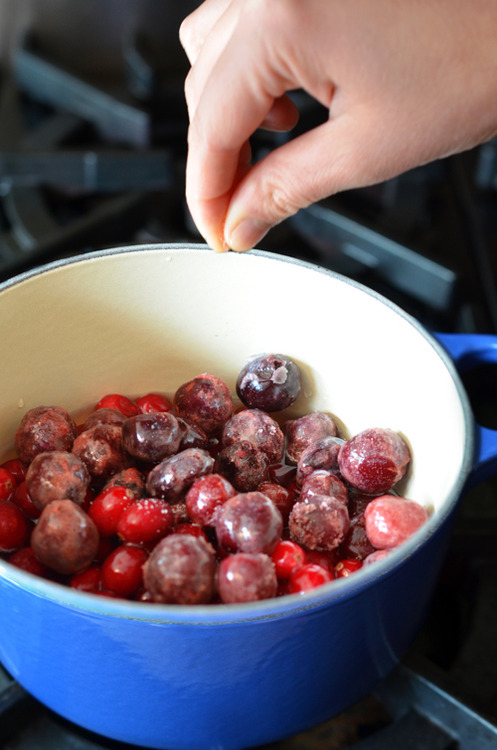 Someone sprinkling salt into a pot filled with cranberries and cherries.
