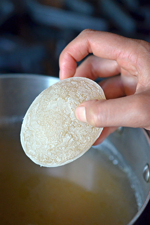 A hand placing a frozen bone broth puck into a pot of bone broth.