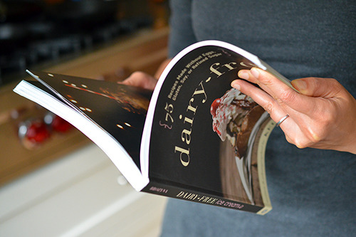 A person is flipping through a copy of Kelly Brozyna’s Dairy-Free Ice Cream cookbook