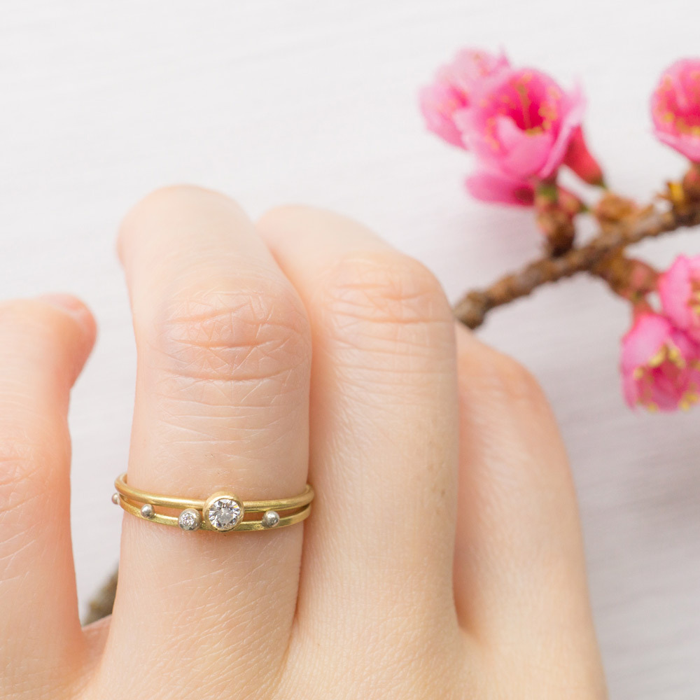 ゴールドのリングをつけた手　桜の花とともに　ダイヤモンド、プラチナ　屋久島でつくる結婚指輪