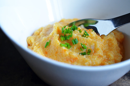 A bowl of Roasted Garlic Autumn Root Vegetable Mash with with a spoon and topped with chives.