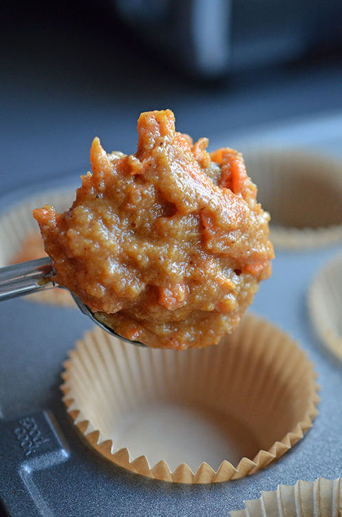 A metal disher is placing Paleo Pumpkin and Carrot Muffin batter into a parchment lined muffin tin.