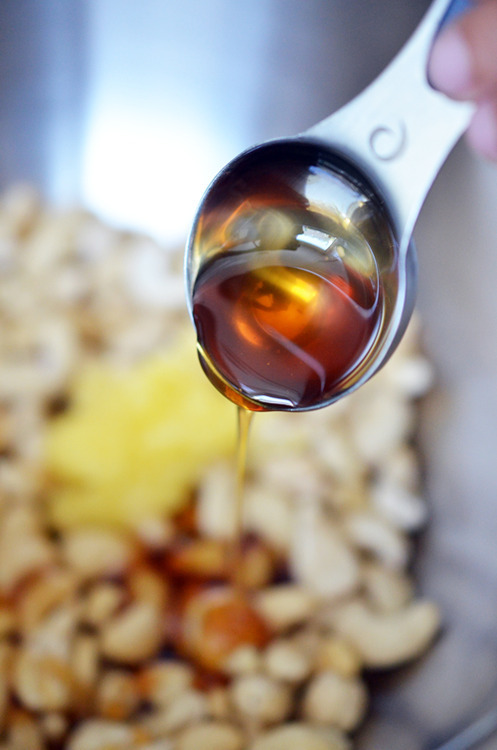 Adding honey into the large metal bowl of cashews.