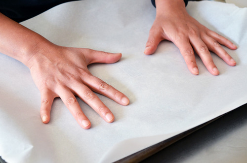 Two hands placing a piece of parchment paper on a rimmed baking sheet to make paleo granola.