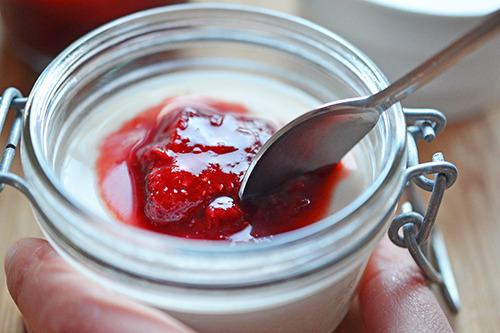 Someone sticking a spoon into a jar of panna cotta with strawberry balsamic compote.