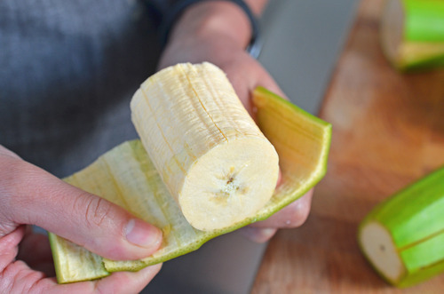 Someone peeling and removing the skin on a chunk of green plantain.