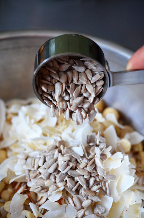Pouring sunflower seeds into a metal bowl filled with the dry ingredients for Tropical Paleo Granola