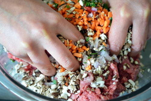 Two hands mixing the ingredients for Asian Meatballs in a bowl.