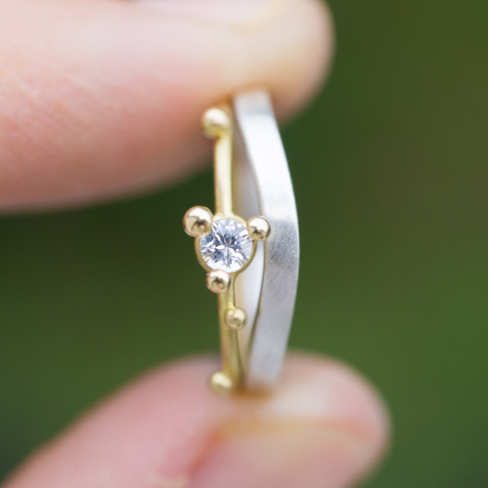 婚約指輪と結婚指輪を重ねる　ゴールド、シルバー、ダイヤモンド　屋久島の緑バック　手に持って