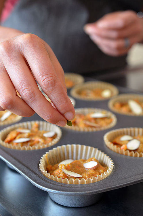 A closeup of a hand placing pipits and almonds on top of uncooked Paleo Pumpkin and Carrot Muffins 