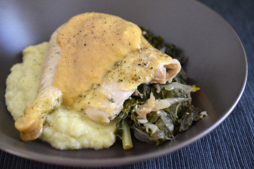 A shot of a chicken leg covered with gravy on a bed of mashed cauliflower and kale. 
