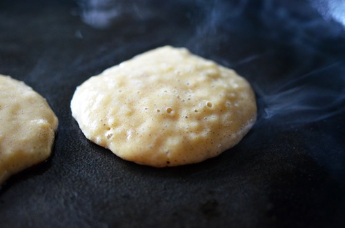 Two cinnamon and coconut paleo pancakes frying off in a pan with steam rising up.