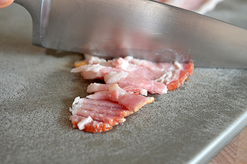 Someone chopping up raw bacon thinly on a cutting board.