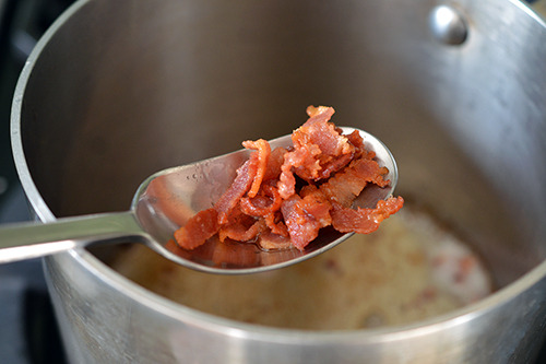 Taking out the fried pieces of bacon out of a small pot with a metal spoon.