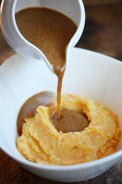 Pouring umami gravy into a bowl of mashed sweet potatoes.