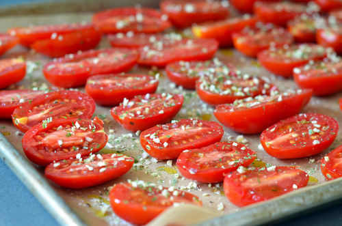 Rows of tomatoes cut in half seasoned with salt and spices and drizzled with olive oil, ready for the oven.