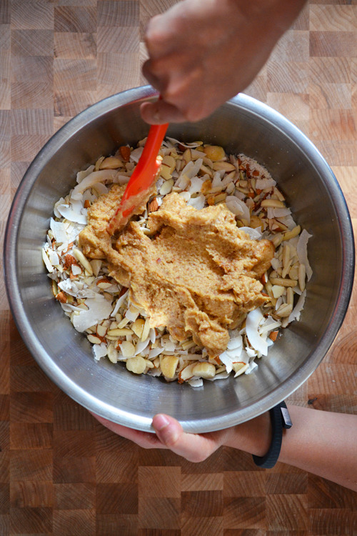 An overhead shot of someone mixing Tropical Paleo Granola with a red silicone spatula