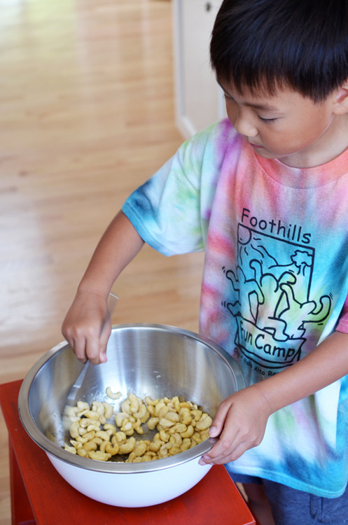 A child mixing together the cashews in a bowl for honey roasted cashews.