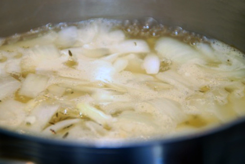 Chicken broth, onions, garlic, and thyme in a saucepan coming to a boil.
