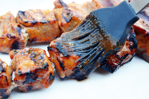 Brushing Whole30-friendly spicy barbecue sauce on grilled pork skewers 