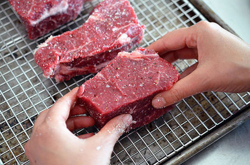 Placing the seasoned strip steaks on a wire rack in a rimmed baking sheet in order to make the perfect steak.