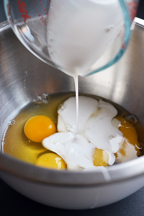 Coconut milk is poured into a mixing bowl filled with eggs.