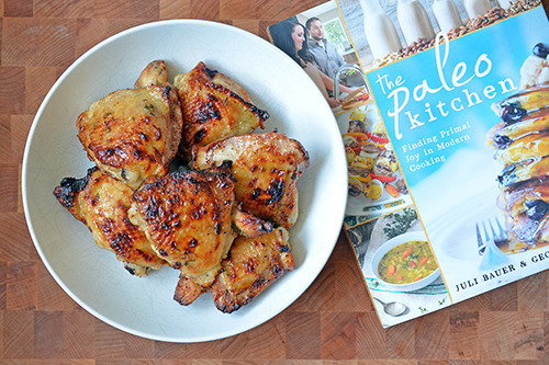 A plate of paleo honey mustard chicken thighs with The Paleo Kitchen cookbook lying next to it.