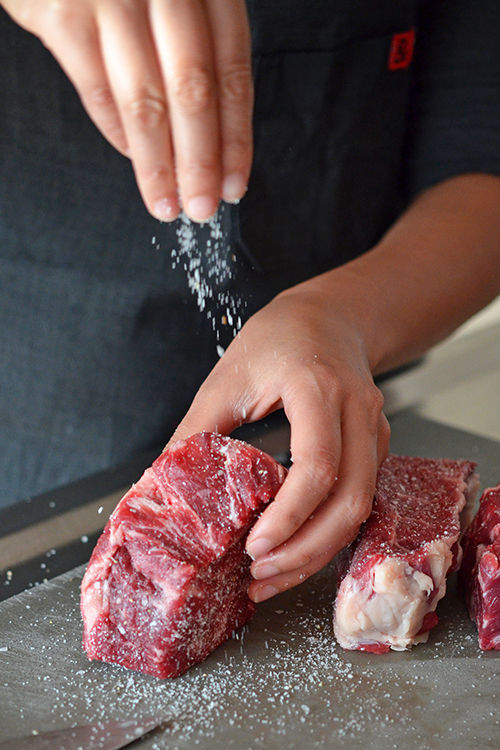 Sprinkling salt and pepper on New York boneless strip steak to season it before cooking.
