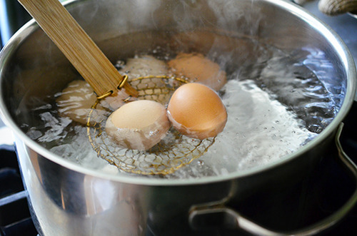 Someone hard boiling eggs in a large pot, taking the eggs out with a spider strainer.