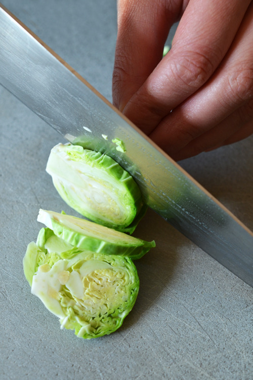 Someone slicing a Brussels Sprout into thin slices for Whole30 Warm Brussels Sprouts Slaw with Asian Citrus Dressing 