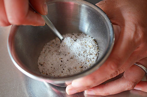 An overhead shot of salt and pepper in a silver bowl with a small spoon inside.