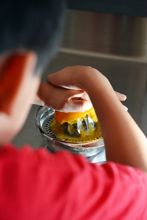 A small boy is juicing an orange on a stainless steel manual juicer.