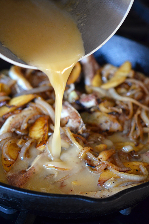 Pouring in the reserved sauce into the cast iron skillet containing the pork chops and sautéed onions and apples.
