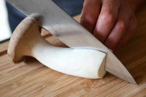Someone slicing a large king oyster mushroom in half.