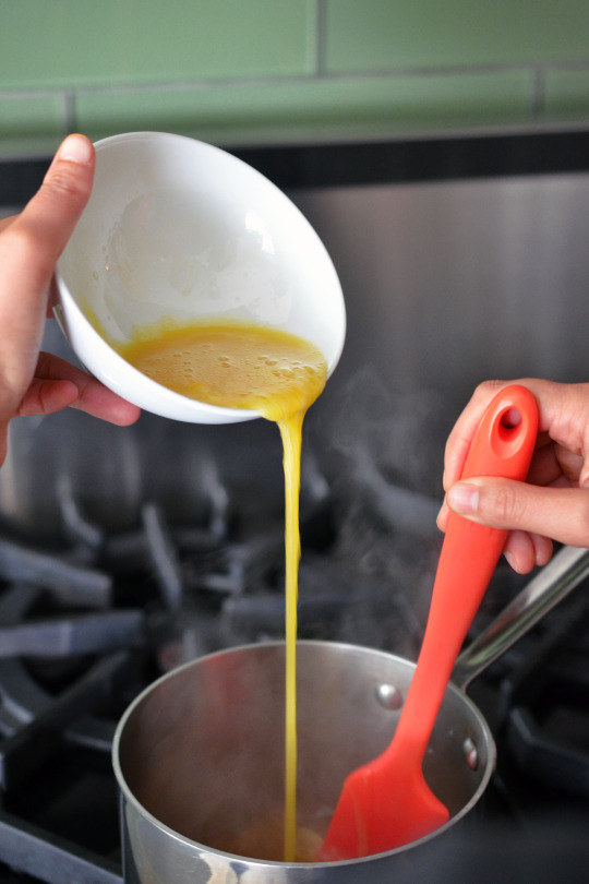 Whisked egg is poured from up high into a small saucepan filled with simmering broth.