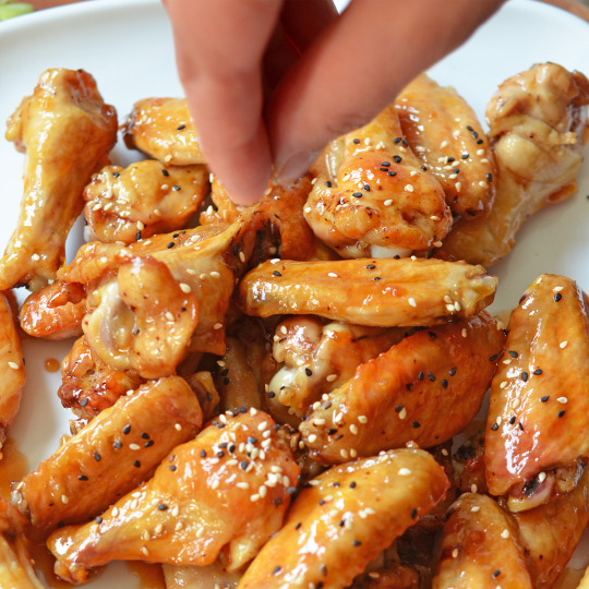 Someone sprinkling sesame seeds on cooked chicken wings.