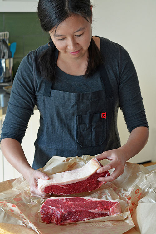 A woman is taking out two thick New York strip steaks on a piece of butcher's paper.