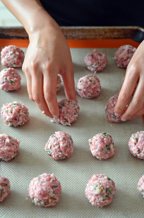 Two hands are shown spacing the meatballs evenly apart on a rimmed baking sheet.