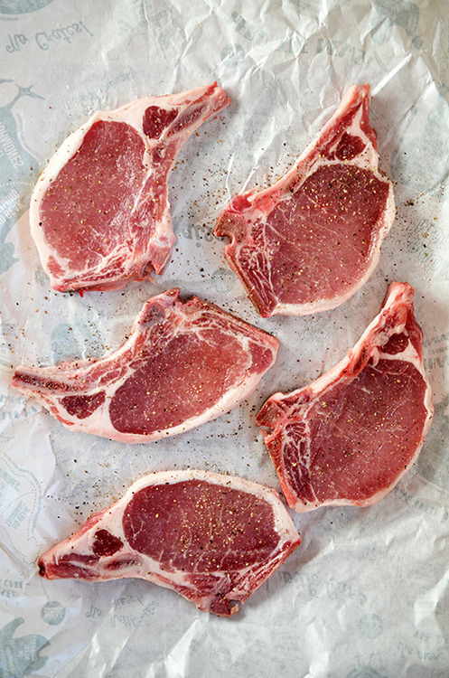 Five pork chops on butcher paper seasoned with salt and pepper.