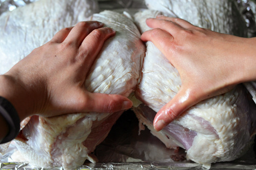 Pressing down on the breast meat of a spatchcock turkey to lay it flat.