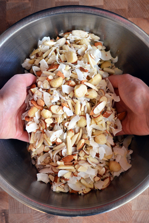 Using hands to toss the nuts and seeds together in a metal bowl for Tropical Paleo Granola