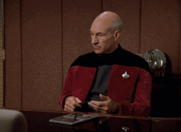 Jean-Luc Picard sitting at a desk playing with a pen and sighing