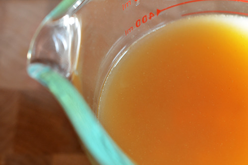 Chicken broth in a glass measuring cup.