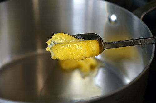 Someone adding a spoonful of ghee to a pot.