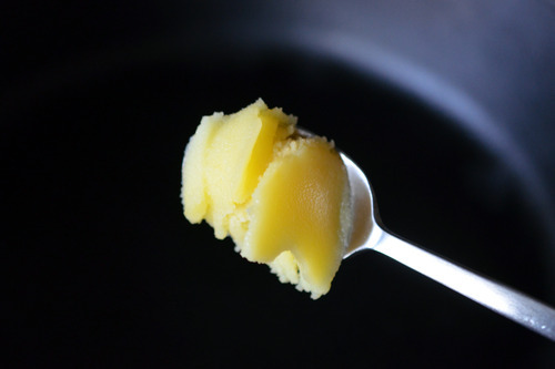 A spoonful of ghee being added to a cast iron skillet.