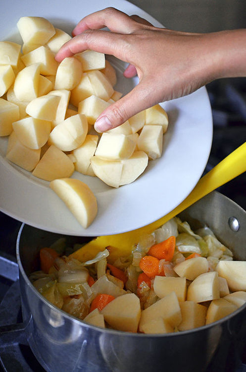 Adding cubed potatoes to a pot.