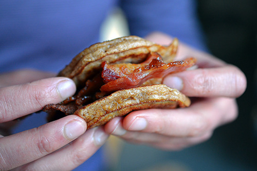 Someone holding a bacon pancake sandwich in their hands.