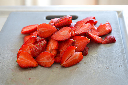 Thinly sliced strawberries on a cutting board.