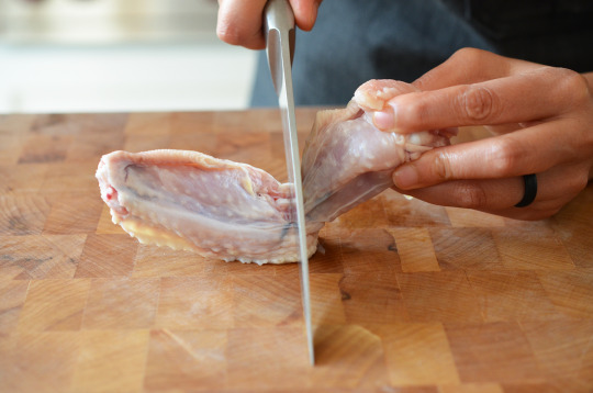 Someone cutting through the joint of a chicken leg.