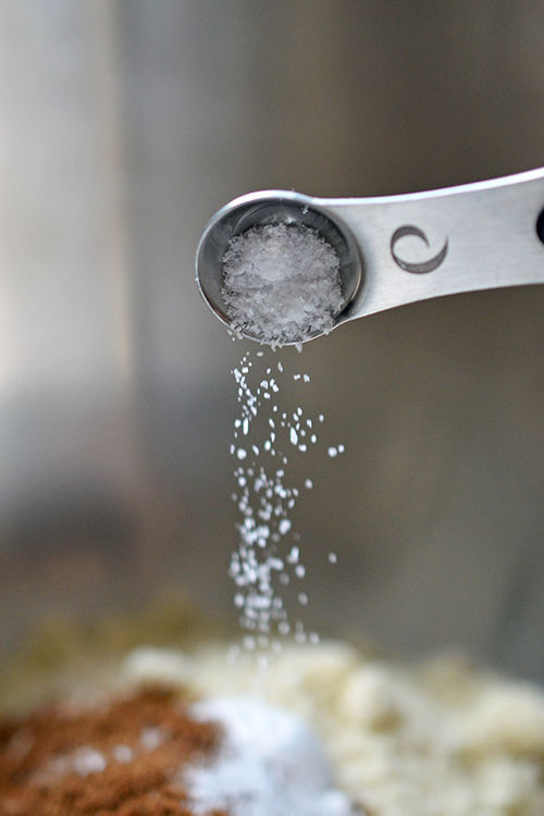 A closeup of a measuring spoon sprinkling salt into a bowl of dry ingredients for Paleo Pumpkin and carrot Muffins 